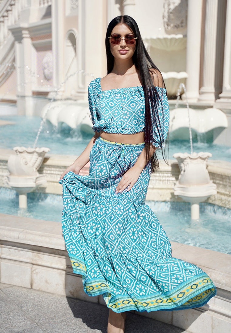 Woman in a blue patterned outfit standing in front of a fountain.