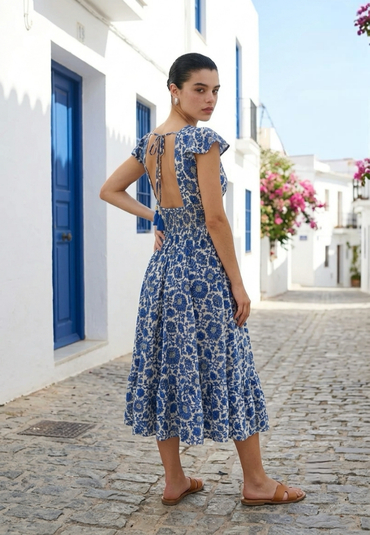 Woman in a blue floral dress standing on a cobbled street in a Mediterranean setting.