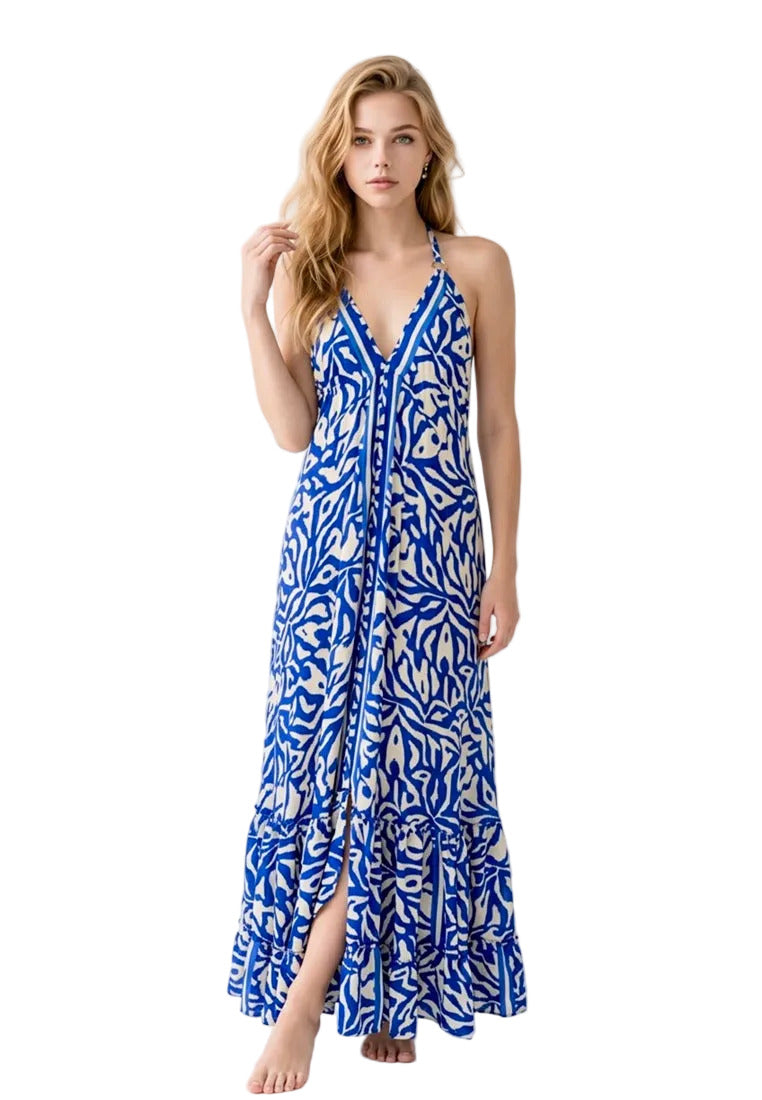 Woman wearing a blue and white patterned silk halter maxi dress from coral secret standing on a stone path with a scenic background