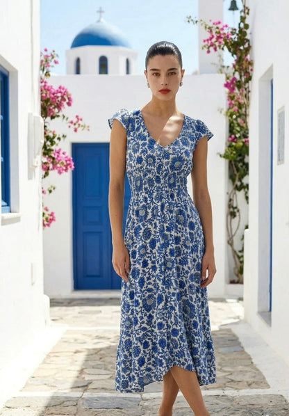 Woman in a blue floral dress standing in a picturesque Mediterranean village setting.
