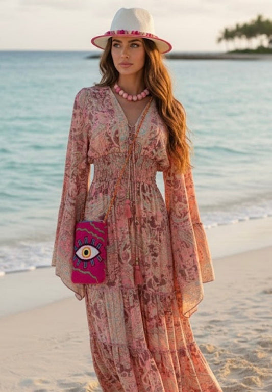 Woman in a floral dress and hat standing on a beach with ocean and sky in the background