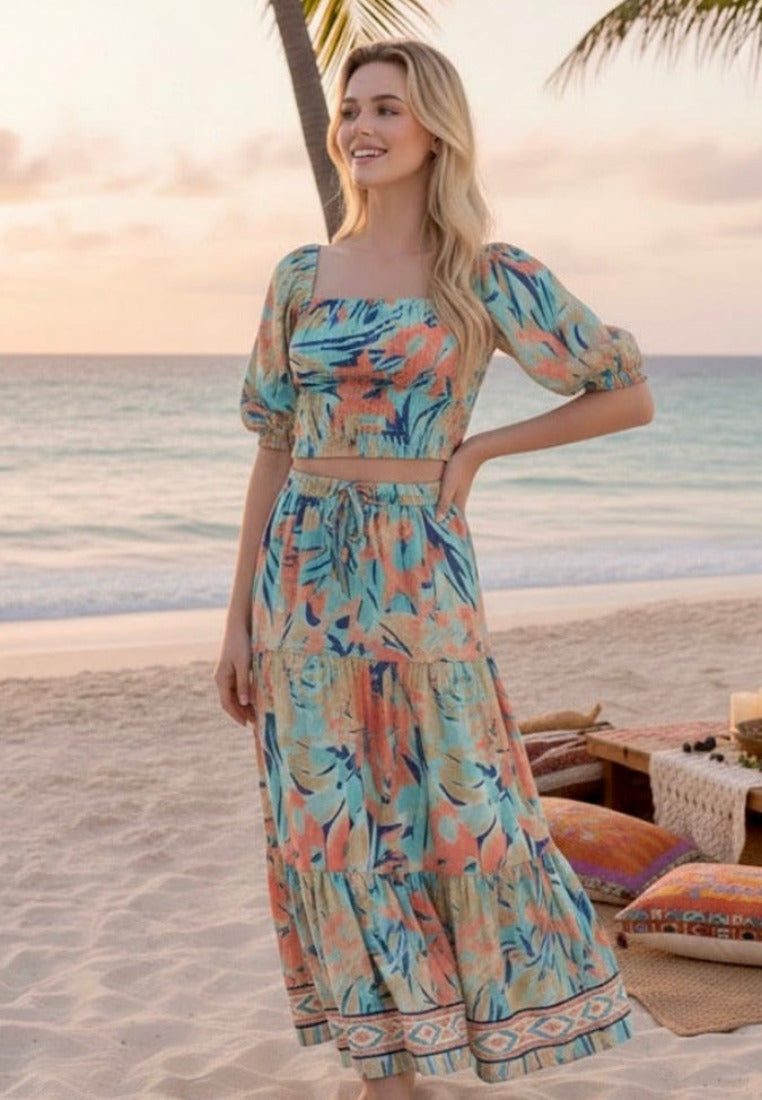 Woman in a floral dress standing on a beach with palm trees and sunset in the background