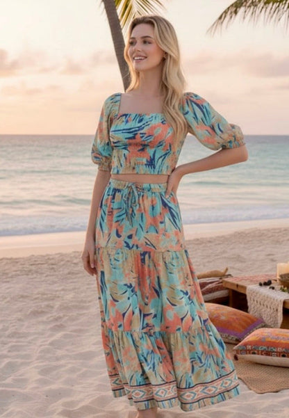 Woman in a floral dress standing on a beach with palm trees and sunset in the background