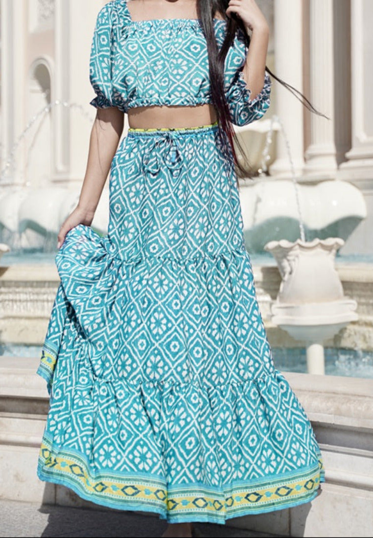 Woman in a blue patterned outfit standing in front of a fountain with classical architecture.