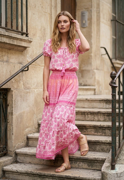 A woman wearing a pink and white patterned maxi dress from coral secret brand