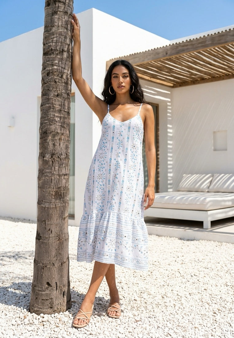 Woman in a white dress standing next to a palm tree in a sunlit outdoor setting