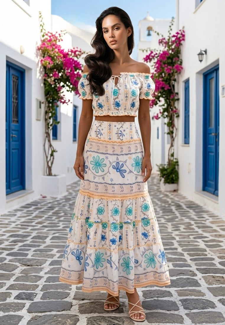 Woman wearing Santorini Flral Crop Top and Midi Skirt co=rd set from Coral SEcret in a picturesque Mediterranean street with flowers 