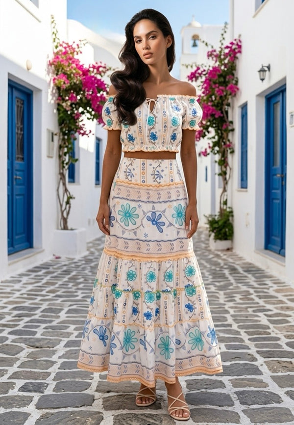 Woman inWoman wearing this Santorini Floral co-ord set from Coral Secretstanding in a picturesque alleyway with blue doors and pink flowers.