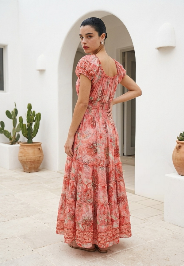 Woman in a floral dress standing in a sunlit outdoor setting with white walls and cacti.