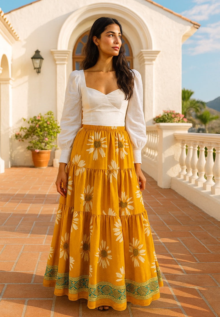 Woman wearing a white top and yellow floral skirt standing in front of a white building with columns.