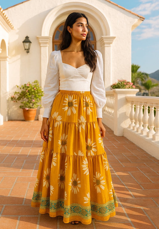 Woman wearing a white top and yellow floral skirt standing in front of a white building with columns.